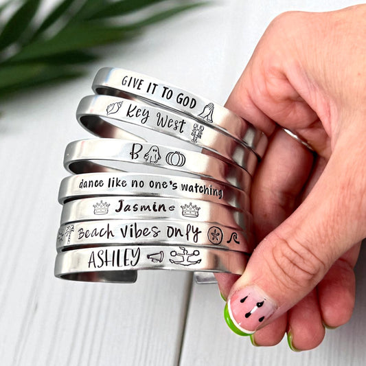 Stack of silver bracelets with various engravings held by a hand on a light background